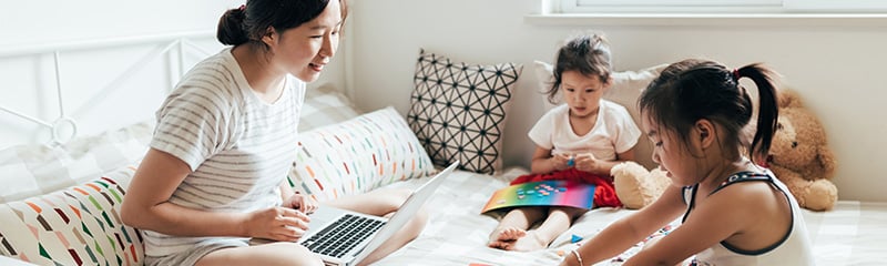 Young mother working at home while her two daughters play