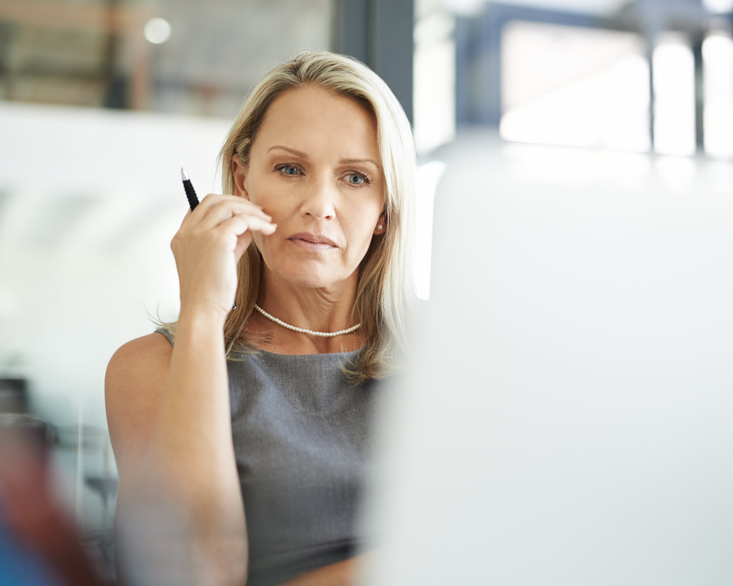 Woman looks at computer with pen in hand